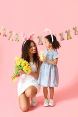 Young African-American woman with tulips, her little daughter and rabbit on pink background