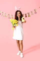 Young African-American woman with tulips and Easter rabbit on pink background