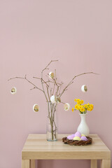 Creative composition with tree branches, Easter eggs and narcissus flowers on table near color wall