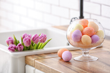 Different Easter eggs and bouquet of tulips in sink on kitchen counter