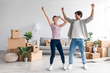 Smiling excited young caucasian family in casual dancing in living room with cardboard boxes, enjoy relocation