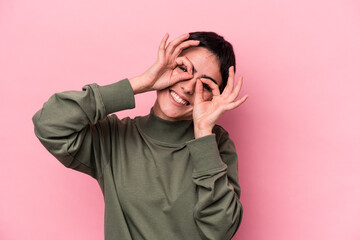 Young caucasian woman isolated on pink background showing okay sign over eyes