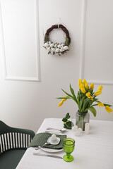 Bouquet of beautiful tulips on served dining table near white wall with Easter wreath