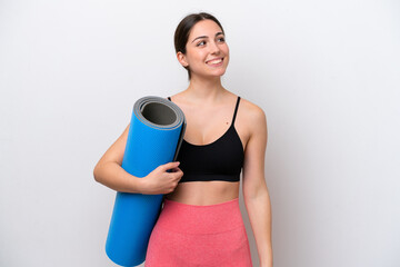 Young sport girl going to yoga classes while holding a mat isolated on white background looking to...