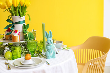 Stylish dinnerware and Easter decor on served table near color wall