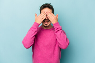 Young caucasian man isolated on blue background covers eyes with hands, smiles broadly waiting for a surprise.