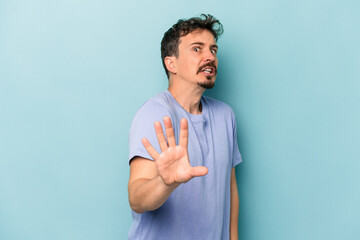 Young caucasian man isolated on blue background being shocked due to an imminent danger
