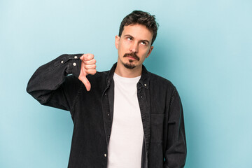 Young caucasian man isolated on blue background showing a dislike gesture, thumbs down....