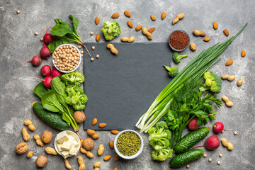 A source of protein for vegetarians. Healthy clean food: greens, vegetables, nuts and legumes top view on a concrete background with a black cutting stone in the center.