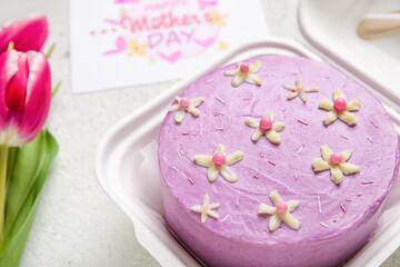Plastic lunch box with tasty bento cake, greeting card and flowers on light background, closeup