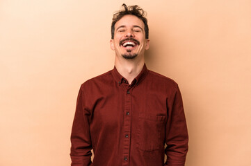 Young caucasian man isolated on beige background relaxed and happy laughing, neck stretched showing teeth.