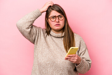Young caucasian overweight woman holding a mobile phone isolated on pink background being shocked,...