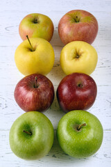 Six multicolored apples on a white wooden background
