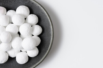 White sugar balls in a ceramic saucer on a white background. Close up top view. Place for text.
