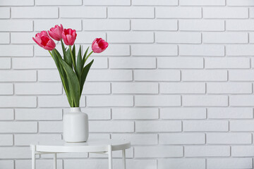 Vase with beautiful tulips on table near white brick wall
