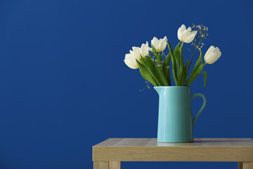 Jug with tulips on table near blue wall