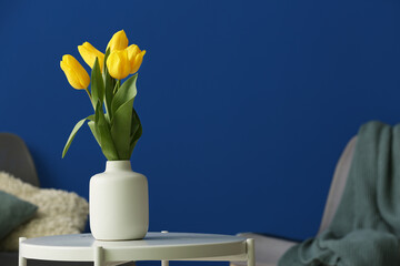 Vase with tulips on table against blue background