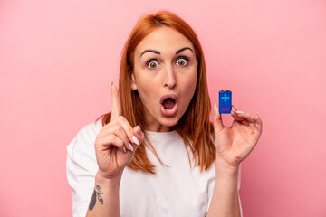 Young caucasian woman holding a batteries isolated on pink background having an idea, inspiration concept.