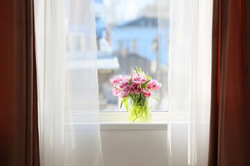 Glass vase with beautiful tulip flowers on windowsill