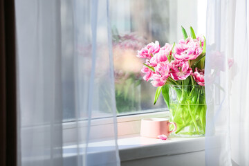 Vase with beautiful tulip flowers and cup of tea on windowsill