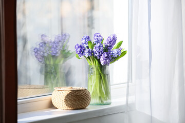 Vase with beautiful hyacinth flowers and wicker bowl on windowsill