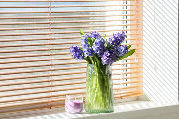 Vase with beautiful hyacinth flowers and candle on windowsill