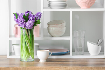 Vase with hyacinth flowers and cup of coffee on kitchen counter