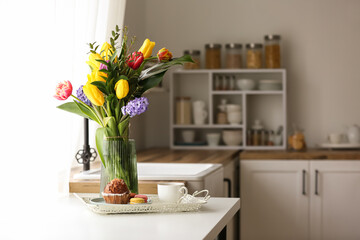 Beautiful flowers and tray with breakfast on table in kitchen
