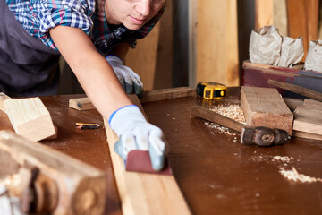 Wood grinding process by sandpaper. Female carpenter using sandpaper on a piece of timber for...