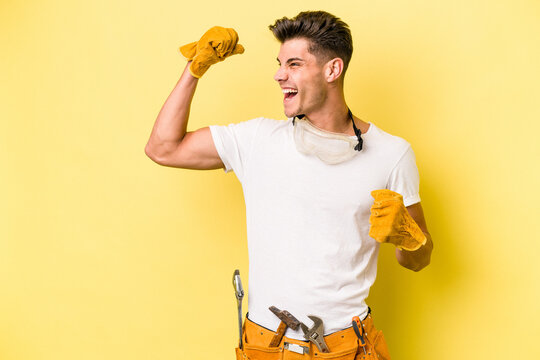 Young electrician caucasian man isolated on yellow background raising fist after a victory, winner concept.