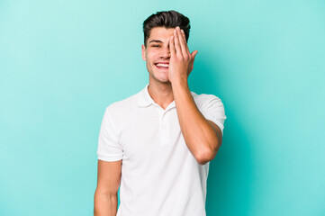 Young caucasian man isolated on blue background having fun covering half of face with palm.