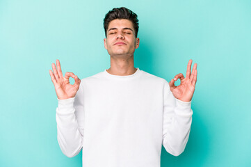 Young caucasian man isolated on blue background relaxes after hard working day, she is performing yoga.