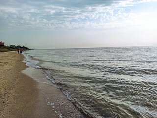 Sea shore. People walk along the shore under the soft rays of the morning sun