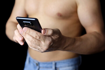 Muscular man in jeans with naked torso with smartphone in hands. Concept of text messaging, online communication