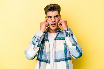 Young caucasian man isolated on yellow background covering ears with fingers, stressed and desperate by a loudly ambient.