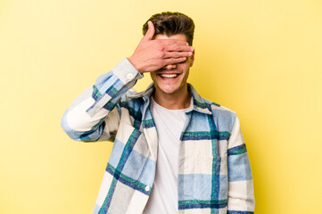 Young caucasian man isolated on yellow background covers eyes with hands, smiles broadly waiting for a surprise.