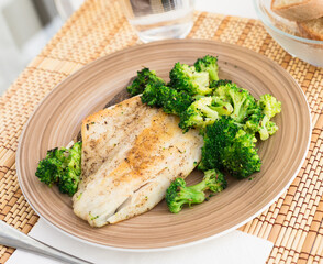 fried fillet of sea bass with garnish of broccoli on black warm stone plate