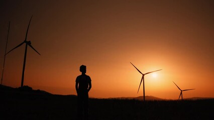 Silhouette Engineer standing on field with windmills. Dreaming of a clean and sustainable future for generations to come, heartwarming uplifting picture of clean energy for the environment.