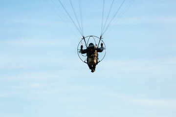 motor paraglider pilot hanging on the straps in the blue sky