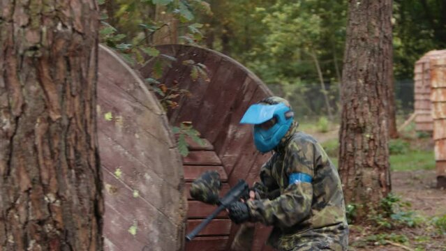 Play paintball game, players with guns. Painterly team in uniform and masks, extreme sport. Opposing teams of players shooting on paintball playing field outdoors. Group of people runs towards enemy