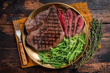 BBQ dinner with top sirloin beef steak and salad on a plate. Wooden background. Top view