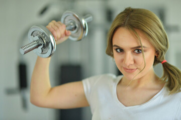 Sporty young woman training with dumbbells  in gym