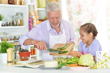 Senior man in chefs uniform preparing dinner with his granddaughter