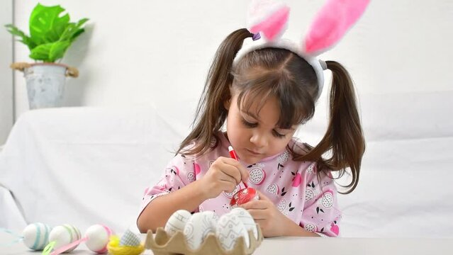 Happy little girl with bunny ears painting the egg with fiberpen, preparing for Happy Easter day.