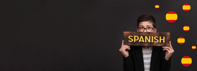 learning Spanish. banner on a black background. a handsome teenager holds an advertising sign. space for copying.