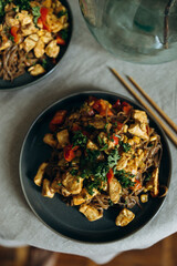 portion of soba noodles with stewed vegetables and meat on a plate top view. plate with brown pasta with chicken fillet pieces, wok vegetables and herbs. asian traditional food top view.	