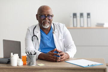 Portrait of smiling doctor looking at camera sitting at desk