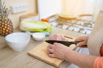 Woman is cooking in home kitchen. Female hands cut fresh Turkey meat on table on wooden boards. Ingredients for preparing food.