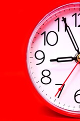 Half of round red classic alarm clock with arrows showing the expiration of time close up on a red background. Vertical frame