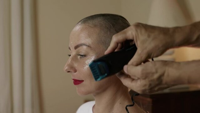 A happy attractive woman is shaved bald with a hair clipper. Close-up of a man's barber's hands.